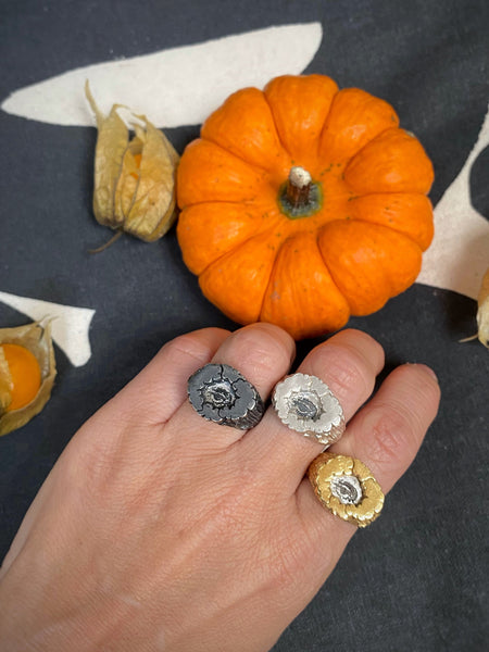 Hand wearing three rings with small pumpkins and green fruits on a patterned background