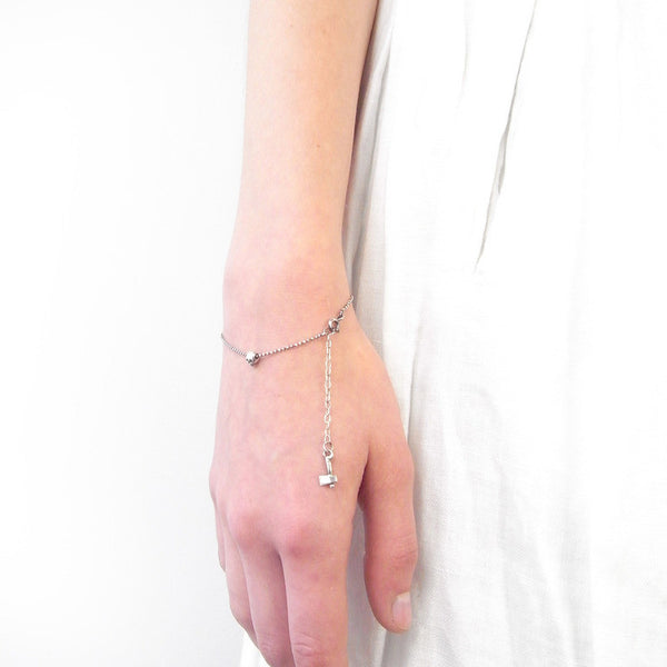 Model wearing a dainty recycled silver tiny skull bracelet, minimalist layering style.
