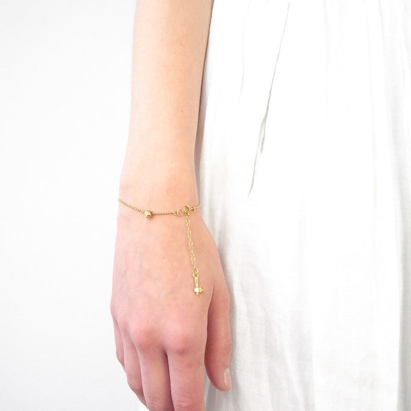 Model wearing a dainty gold vermeil recycled silver tiny skull bracelet, minimalist layering style.
